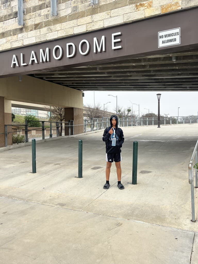 Vonzelle Brown II with his Navy National Combine credential, standing under the Alamodome sign in San Antonio